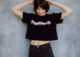 A model wearing a black cropped t-shirt featuring a millipede in a ghost costume carrying jack o'lantern candy pails. 