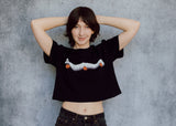A model wearing a black cropped t-shirt featuring a millipede in a ghost costume carrying jack o'lantern candy pails. 