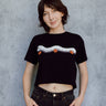 A model wearing a black cropped t-shirt featuring a millipede in a ghost costume carrying jack o'lantern candy pails. 
