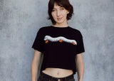 A model wearing a black cropped t-shirt featuring a millipede in a ghost costume carrying jack o'lantern candy pails. 