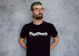 A model wearing a black t-shirt with a hand drawn illustration of a millipede in a ghost costume carrying jack'o lantern candy pails. 