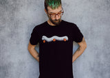 A model wearing a black t-shirt with a hand drawn illustration of a millipede in a ghost costume carrying jack'o lantern candy pails. 