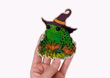 A hand holding a holographic sticker featuring a toad in a witch hat with pumpkins.