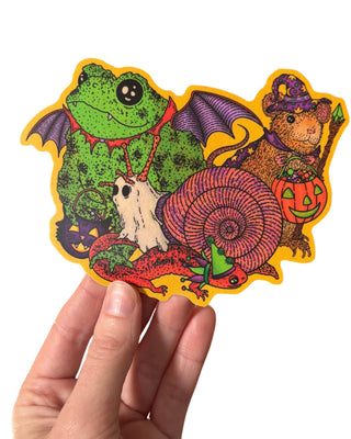 A hand holding a sticker featuring various animals trick or treating in retro style costumes for halloween. 