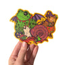 A hand holding a sticker featuring various animals trick or treating in retro style costumes for halloween. 